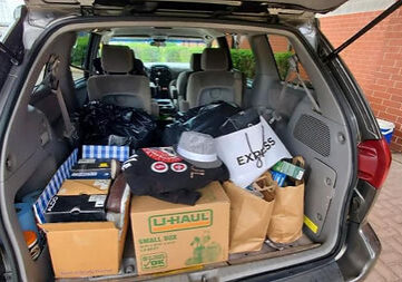An SUV trunk open with boxes of clothes, shoes, and other items needed for the work place.